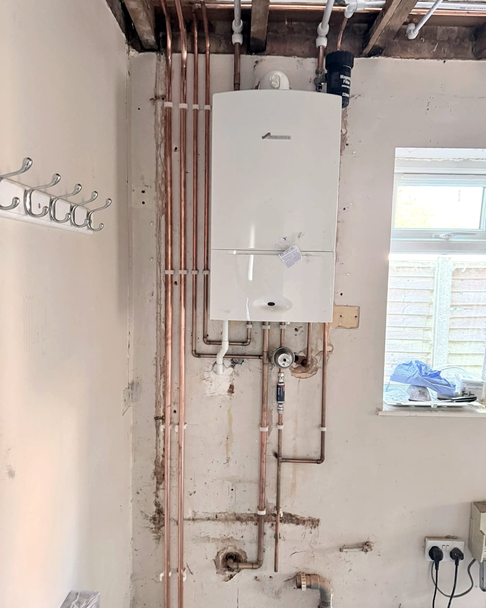 New copper and plastic pipe runs clipped between open ceiling joists above a freshly fitted boiler