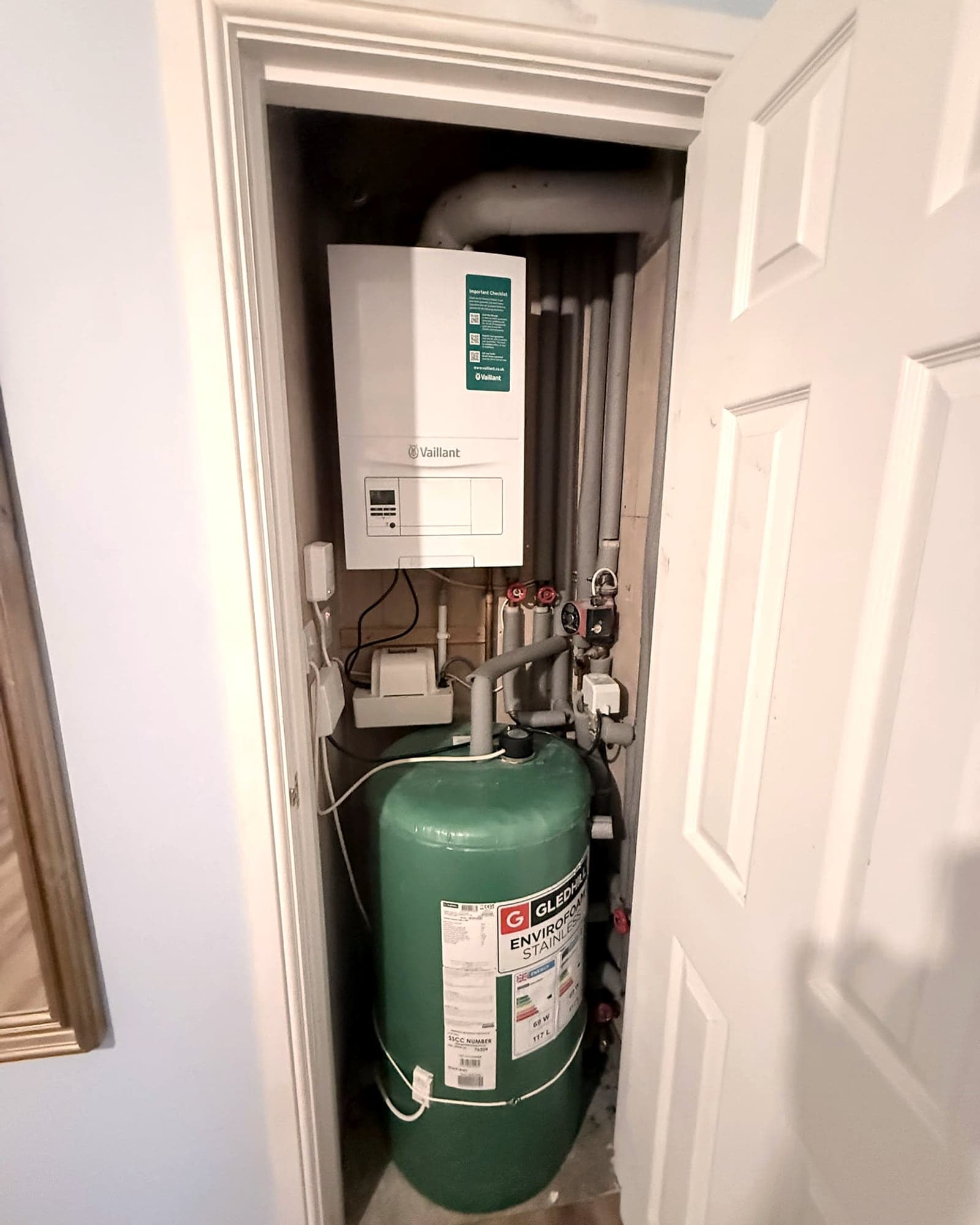 A wall-hung Vaillant boiler above a green hot water cylinder in an airing cupboard